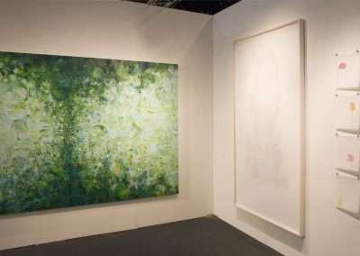 An art gallery corner showing a large, vibrant green abstract painting on the left and a tall, white textured artwork on the right, along with smaller red and pink pieces on an adjacent wall.