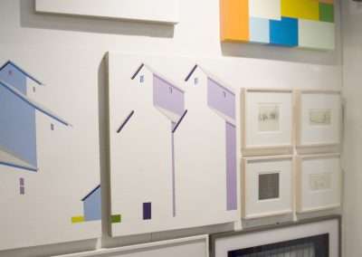 An art gallery wall displaying a variety of framed artworks including a cable car, abstract color blocks, minimalist houses, and densely packed floral patterns.