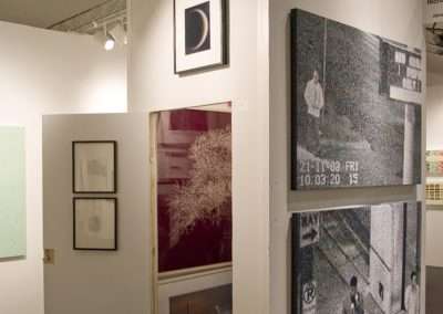 An art gallery installation featuring a large, cube-shaped structure displaying black and white photographs and a partially open door on the left side revealing additional contemporary art pieces inside.