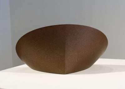 A large, elliptical bronze sculpture with a textured surface, displayed on a white pedestal against a neutral background.
