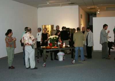 Group of people mingling and enjoying refreshments at an art gallery opening reception.
