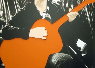 A stylized graphic of a person playing an orange guitar, with the image emphasizing bold colors and minimal details against a monochrome background, reminiscent of contemporary art.