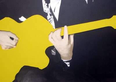 A close-up image of a person in a dark suit playing a bright yellow guitar, focusing on the hands strumming the strings, evoking the style of conceptual artist John Baldessari.