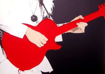 A graphic art depiction of a person with obscured facial features playing a vibrant red electric guitar. The image is stylized with high contrast colors, mainly red, white, and black.