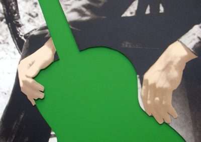 A black and white cutout image by visual artist John Baldessari, depicting a person holding a guitar, with the guitar colored in bright green. Only the torso and hands of the person are visible.