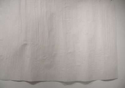 A large, textured white paper with a grid of creases displayed on a gallery wall, evoking a minimalist artistic style.