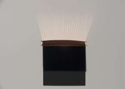 A book with a copper-colored cover opened slightly at the top, creating a fan-like spread of light rays shining upward against a plain background.