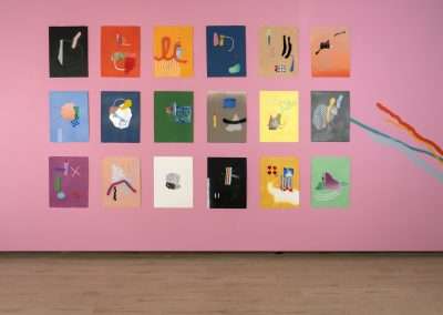 An art exhibition wall showcasing a collection of 20 abstract paintings of various vibrant colors, mounted on a pink background. Each painting features unique shapes and forms.