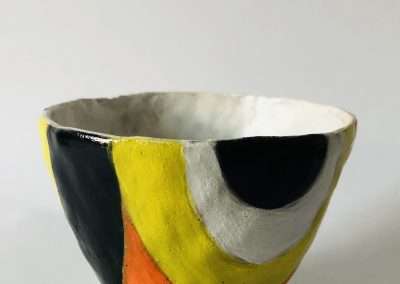 A colorful ceramic bowl featuring abstract sections painted in black, white, yellow, and orange on a light gray background, showcasing some of my favorite things.