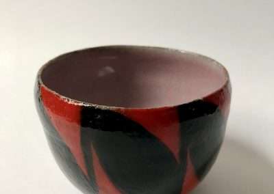 A handcrafted ceramic bowl with a matte finish, featuring an abstract design in red and black over a grey background. The bowl, one of my favorite things, is displayed against a plain white surface.