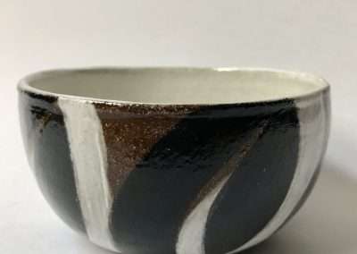 A ceramic bowl with a glossy finish, featuring our favorite abstract pattern in shades of black, white, and metallic gold on a light gray background.