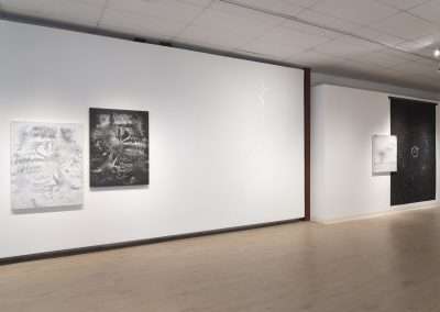 Modern art gallery interior displaying four large contemporary art pieces on plain white walls, with soft lighting and a polished wooden floor.