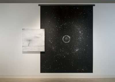 Art gallery interior showcasing two abstract paintings: on the left, a smaller canvas with marble-like textures by Shoshannah White; on the right, a larger piece depicting a starry galaxy with a spiral formation.