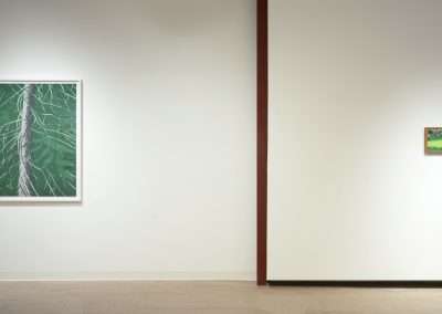 A minimalist art gallery displays two framed paintings on a clean white wall. The left painting depicts green foliage with white branches, while the smaller right painting features a landscape with greenery. Both are separated by a vertical dark red line.