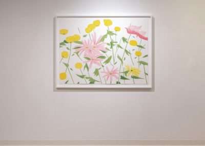 A minimalist art gallery displays a framed painting of pink and yellow flowers on green stems against a white background. The artwork is centered on a plain, light-colored wall and illuminated by two overhead lights, with a wooden floor below.