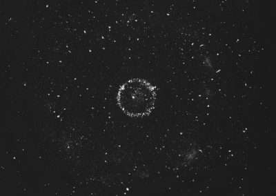 A grayscale image of a starry night sky featuring numerous scattered stars. At the center is a distinct, circular formation of stars, appearing like a cosmic wreath or ring, against a deep black background. The overall effect is mesmerizing and serene.