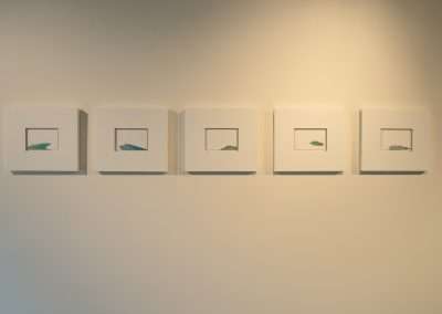 A series of five minimalist framed artworks displayed on a light-colored wall at Bishop's Lodge. Each frame contains a simple, abstract image in muted tones, possibly depicting aquatic shapes reminiscent of Eric Tillinghast's style. The frames are evenly spaced and uniformly sized.