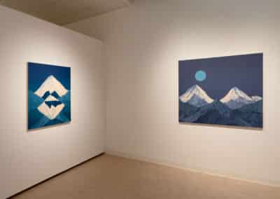 A minimalist art gallery features two paintings of snowy mountains. The left painting depicts a single snow-capped peak with its reflection, while the right painting shows two snow-covered mountains under a blue sky with a full moon. The gallery walls and floor are white.