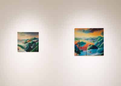 Two vibrant landscape paintings are displayed on a plain wall in an art gallery. The left painting depicts a serene, mountainous scene at sunset, while the right painting showcases a coastal scene with colorful hills under a dynamic sky. Both are well-lit.