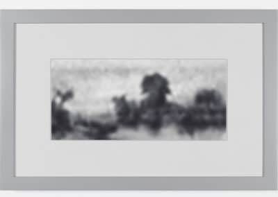 A framed artwork features a grayscale, blurry landscape. The indistinct image appears to depict trees and possibly a body of water, with a hazy sky above. The photograph is surrounded by a simple, light gray frame.