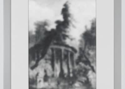 A framed black and white photograph of a blurred landscape featuring a forest scene. Tall trees surround a small, ancient-looking structure with columns in the center of the image. The overall look is soft and indistinct.