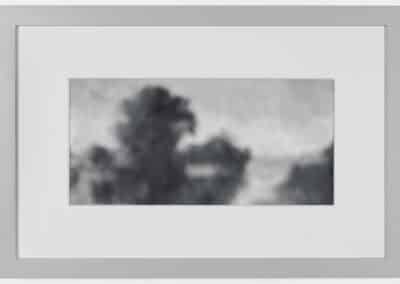 A black-and-white, blurry photograph in a white mat and silver frame, featuring an indistinct landscape with undefined shapes resembling trees or clouds. The image has a soft, abstract quality, evoking a sense of mystery.